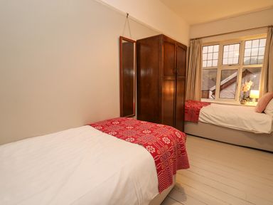 A bedroom with two single beds a wooden wardrobe a full length mirror and a window with curtains at Tirallen in Llangadog