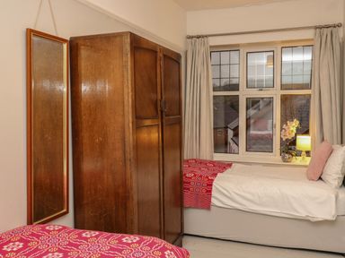 A bedroom with two single beds a wooden wardrobe a mirror and a window with curtains at Tirallen in Llangadog