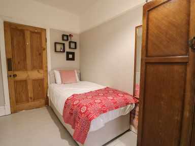 A small bedroom with a single bed wooden door wall shelves and a wooden wardrobe at Tirallen in Llangadog