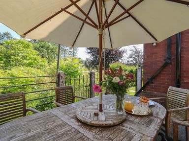 An outdoor wooden table with a white umbrella and chairs with flowers a jug of juice and croissants on the table at Tirallen in Llangadog
