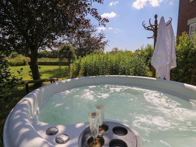 An outdoor hot tub with two champagne glasses and towels on a stand in a garden at Tirallen in Llangadog