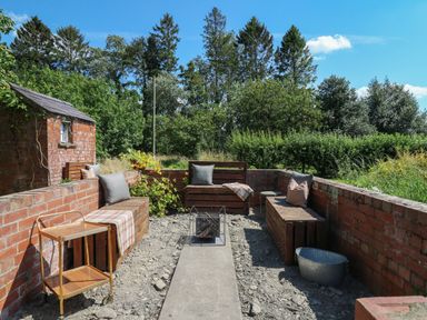 An outdoor seating area with wooden benches and cushions surrounded by brick walls and greenery at Tirallen in Llangadog
