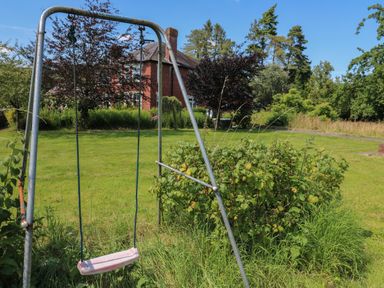 A garden with a metal swing set and a red brick house in the background at Tirallen in Llangadog