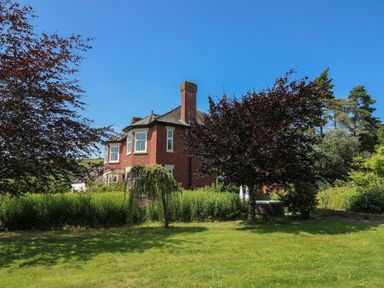 A brick house with a chimney surrounded by green trees and a grass lawn at Tirallen in Llangadog