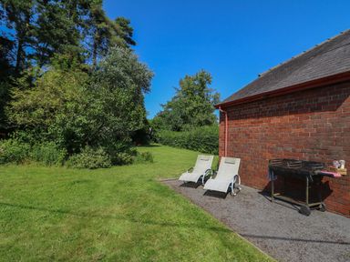 A garden area with two lounge chairs and a barbecue next to a brick building at Tirallen in Llangadog