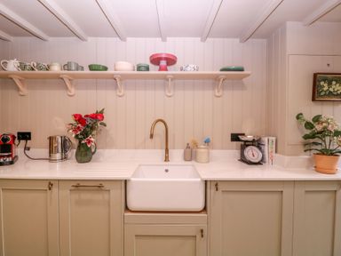 A kitchen with a sink, faucet and dishware on a shelf at Mallards in Bourton-On-The-Water