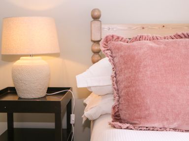 A bedside table with a lamp and a pink pillow at Mallards Bourton-On-The-Water