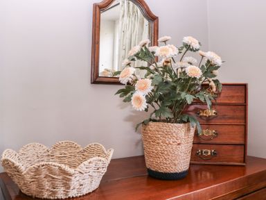 A table with artificial flowers in a woven basket and a mirror at Mallards in Bourton-On-The-Water