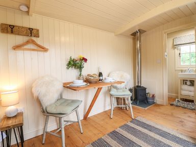 A small dining area with two chairs a wooden folding table and a stove in a room at High Grounds Shepherd's Hut Boylestone near Ashbourne