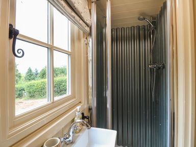 A bathroom with a window beside a sink and a shower area with corrugated metal walls at High Grounds Shepherd's Hut Boylestone near Ashbourne