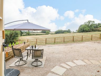 A patio area with table chairs and umbrella overlooking a fenced field at High Grounds Shepherd's Hut in Boylestone near Ashbourne