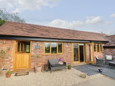 A brick building with wooden doors and windows and outdoor seating at The Old Piggery in Defford
