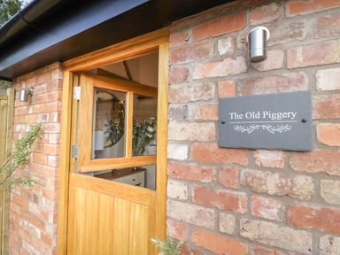 Half wooden door open on a brick wall with a sign reading The Old Piggery at The Old Piggery in Defford
