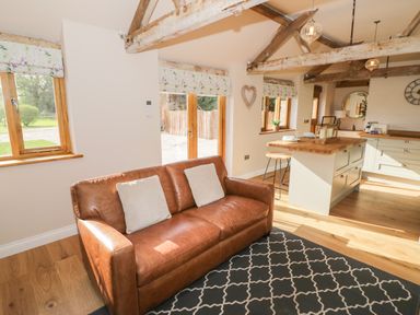 A living area with a brown leather sofa and kitchen island with stools at The Old Piggery in Defford