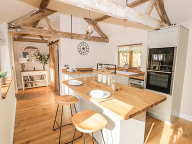 A kitchen with wooden beams and stools at a wooden island counter at The Old Piggery in Defford
