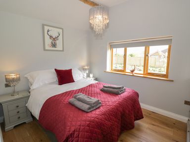 A bedroom with a bed covered in a red quilt and cushions with two bedside tables and lamps at The Old Piggery in Defford
