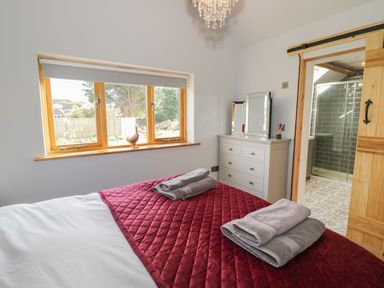 A bedroom with a bed covered in a red quilt and folded towels on top next to a window and a dresser with mirrors at The Old Piggery in Defford