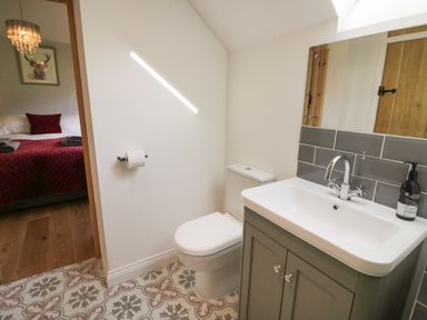 A bathroom with toilet sink and mirror and a bedroom with bed and chandelier visible at The Old Piggery in Defford