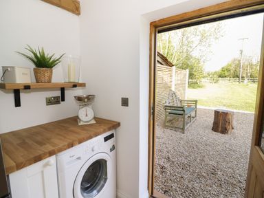 A utility room with a washing machine wooden countertop a shelf with a plant and candle outside a gravel area with a bench and tree stump at The Old Piggery in Defford