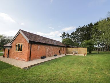 A brick house with a pitched roof and a gravel path surrounded by grass and trees at The Old Piggery in Defford