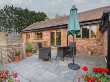 An outdoor patio area with a round table two chairs and a closed umbrella at The Old Piggery in Defford