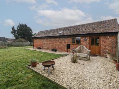 Exterior view of a brick building with wooden door and window with gravel seating area and grass lawn at The Old Piggery in Defford