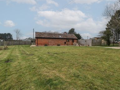 A lawn with a brick building and wooden fence under a cloudy sky at The Old Piggery in Defford