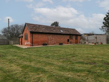 A brick building with a grass lawn and a fence around it at The Old Piggery in Defford