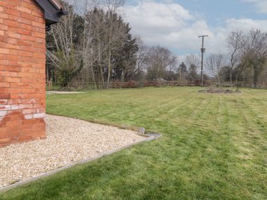 A grassy yard with a flower bed and a brick wall on the left at The Old Piggery in Defford