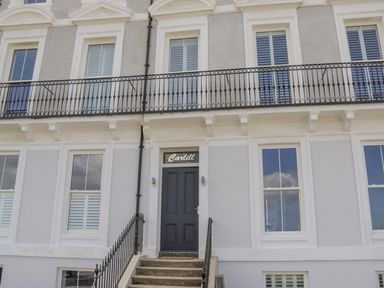 The front entrance of a building with stairs leading to a black door with the word Carlill above and windows on both sides Foxton Penthouse Whitby