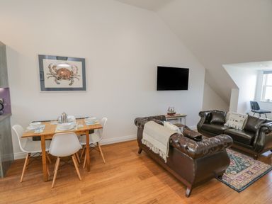 A dining table with four chairs set with plates and cutlery next to two brown leather sofas and a wall-mounted TV at Foxton Penthouse in Whitby