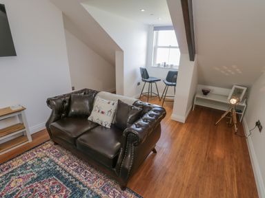A room with a leather sofa cushions two stools by a window a small white shelf with a lamp and a decorative bowl at Foxton Penthouse in Whitby