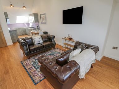 A living room with two brown leather sofas, a colorful rug, a wall-mounted TV, and a small table with a model ship at Foxton Penthouse in Whitby