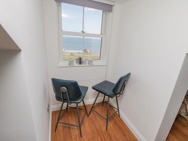 A small dining area with two blue chairs and a glass table by a window overlooking the sea at Foxton Penthouse in Whitby