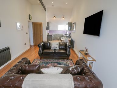 A living room with brown leather sofas a rug and a wall mounted television with a kitchen and dining area in the background at Foxton Penthouse in Whitby