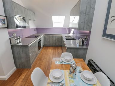 A kitchen with wooden flooring grey cabinets and a dining table set for three at Foxton Penthouse in Whitby