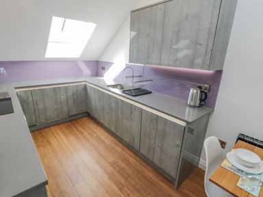 A kitchen with gray cabinets wooden floor a skylight and a dining table with dishes at Foxton Penthouse in Whitby