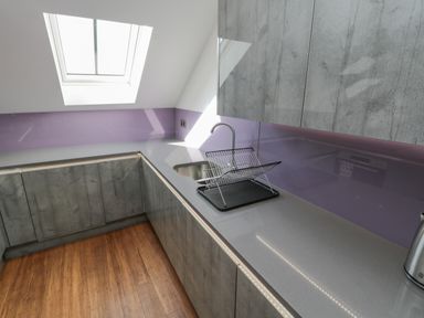A kitchen with grey cabinets a skylight a countertop with a drying rack and wooden floor at Foxton Penthouse in Whitby