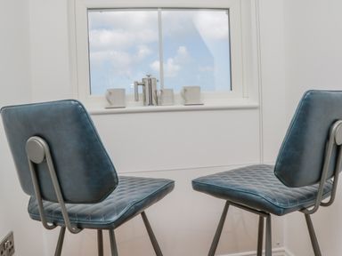 Two blue cushioned chairs facing a window with white cups and a metal coffee press on the windowsill at Foxton Penthouse in Whitby