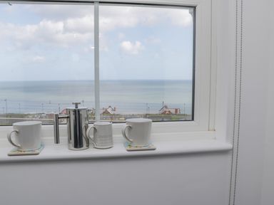 A window sill with two mugs and a metal French press overlooking the sea at Foxton Penthouse in Whitby