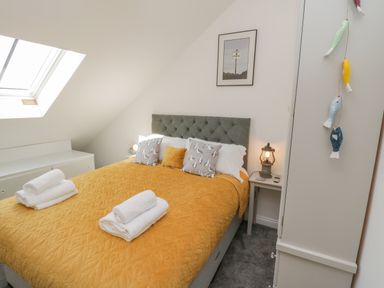 A bedroom with a bed covered in a yellow quilt and white towels on top at Foxton Penthouse in Whitby