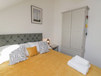 A bedroom with a grey upholstered headboard a yellow bedspread and pillows with seagull patterns a grey wardrobe and a bedside table with a lantern lamp at Foxton Penthouse in Whitby