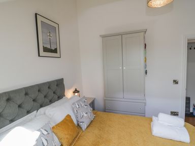 A bedroom with a grey tufted headboard bed with yellow and white bedding next to a grey wardrobe at Foxton Penthouse in Whitby