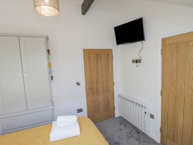 A bedroom corner with a mounted television radiator two wooden doors a bed with towels and a wardrobe at Foxton Penthouse in Whitby