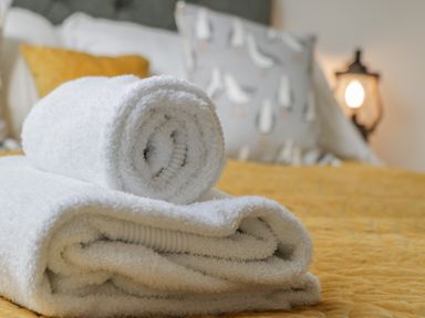 A bed with stacked white towels and pillows including one with a bird pattern on a yellow bedspread at Foxton Penthouse Whitby