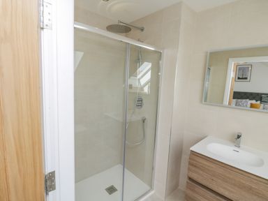 A bathroom with a glass shower enclosure and a wooden vanity with a white sink at Foxton Penthouse in Whitby