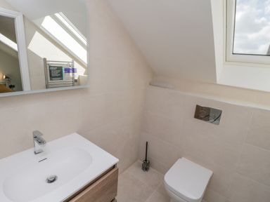A bathroom with a white sink and faucet a mirror a toilet with dual flush buttons a toilet brush and a window at Foxton Penthouse in Whitby