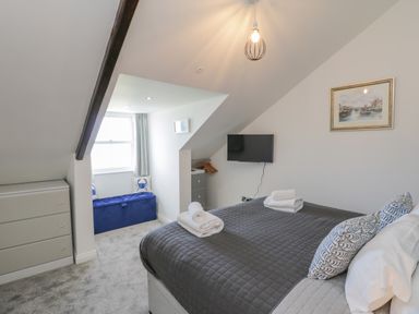 A bedroom with a gray bedspread a wall-mounted TV a blue storage bench and a dresser at Foxton Penthouse in Whitby