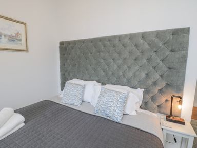 A bedroom with a large tufted headboard pillows and a bedside table with a lamp at Foxton Penthouse in Whitby