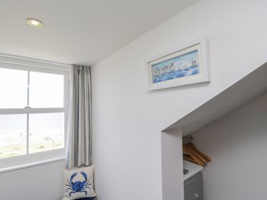 A corner of a room with a window, striped curtains, a pillow with a blue crab design, a framed picture on the wall, and a space with wooden hangers at Foxton Penthouse in Whitby